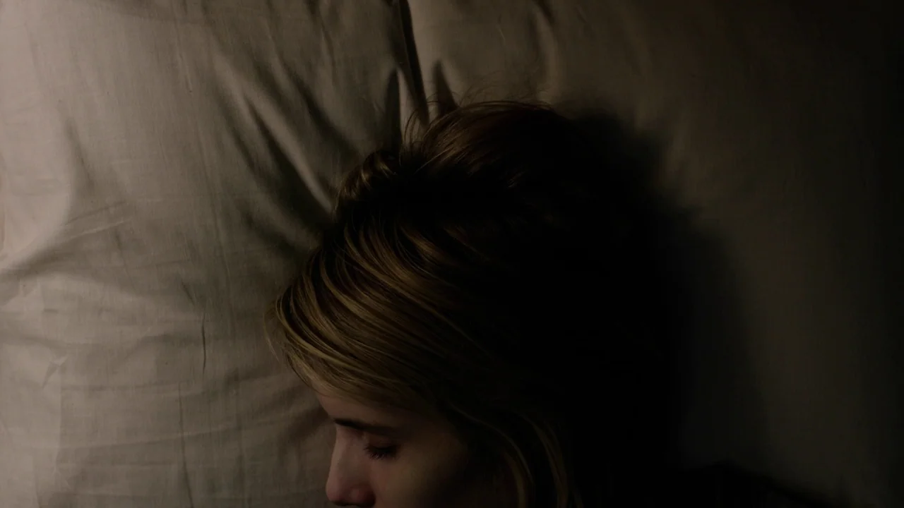 The Blackcoat’s Daughter (2015) movie still: closeup — A close overhead view shows a person's head resting on a crumpled white pillow. The subject…