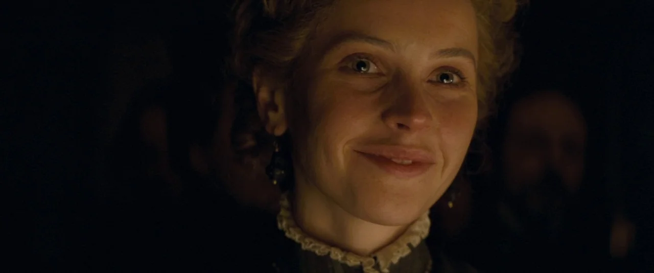 The Invisible Woman (2013) movie still: closeup — A woman stands in a dimly lit, dark environment during the 19th century. She smiles while looking…