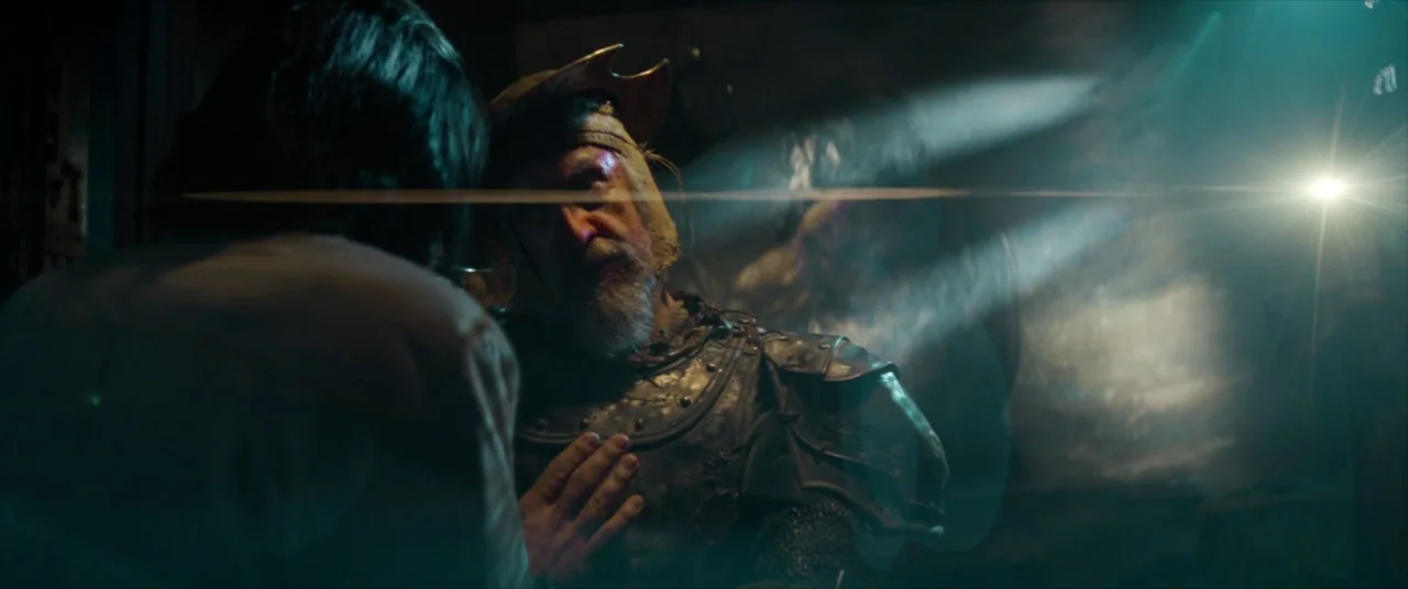 The Man Who Killed Don Quixote (2018) movie still: medium — A dimly lit stone chamber fills with dust motes and intense horizontal light flares. An…