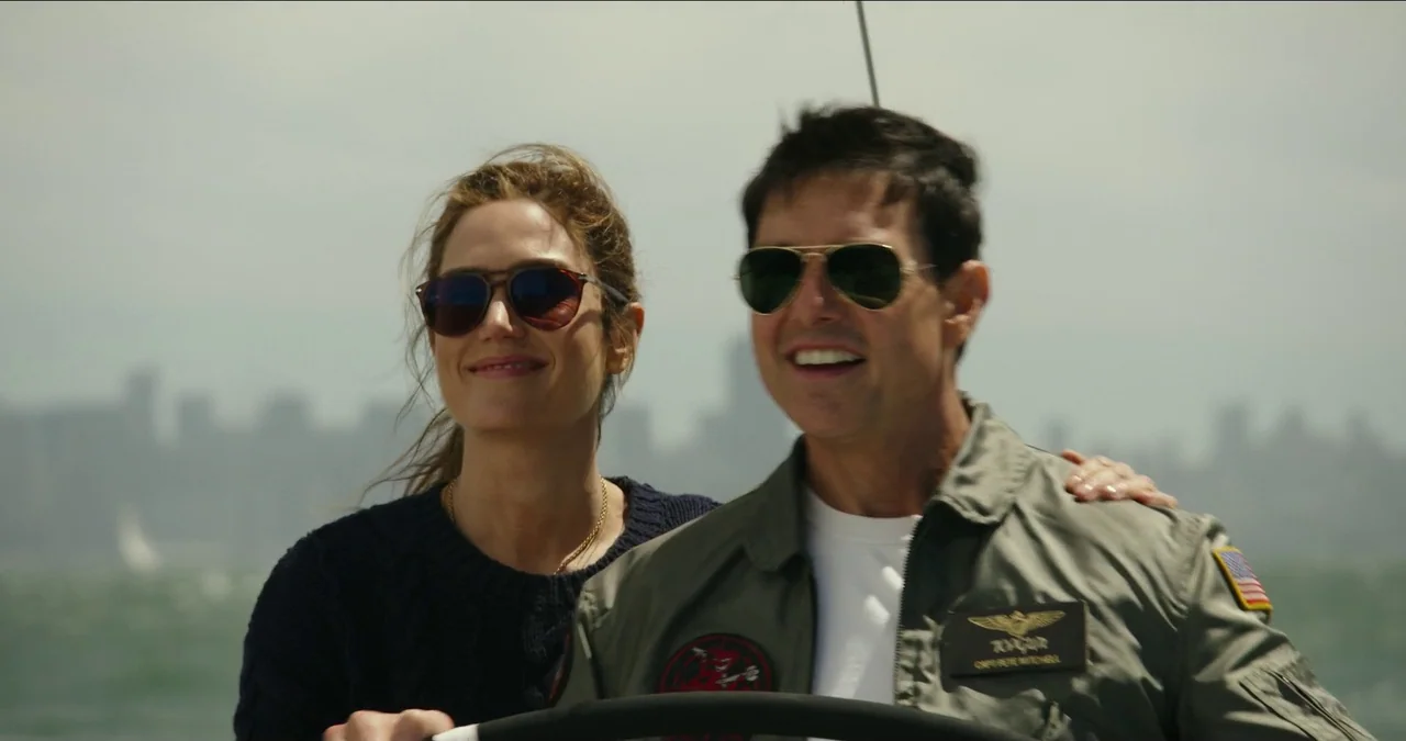 Top Gun: Maverick (2022) movie still: medium — A man and woman sail on water with a blurred cityscape in the background. The man wears a flight…
