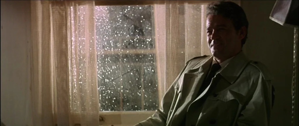 The Graduate (1967) movie still: medium — A dimly lit room features a window with curtains and visible rain droplets outside. A middle-aged man in a…