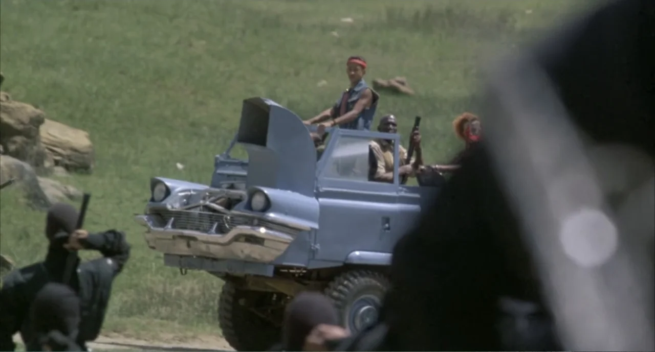 American Ninja 4: The Annihilation (1990) movie still: wide — A modified blue vehicle travels across a bright green open grassy field area. Several…