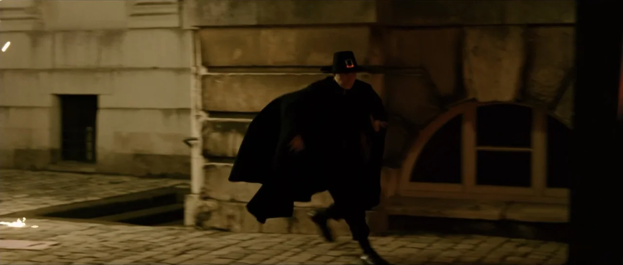 The Oxford Murders (2008) movie still: fullbody — A stone-paved courtyard sits at night adjacent to a building with an arched window. A man in a…