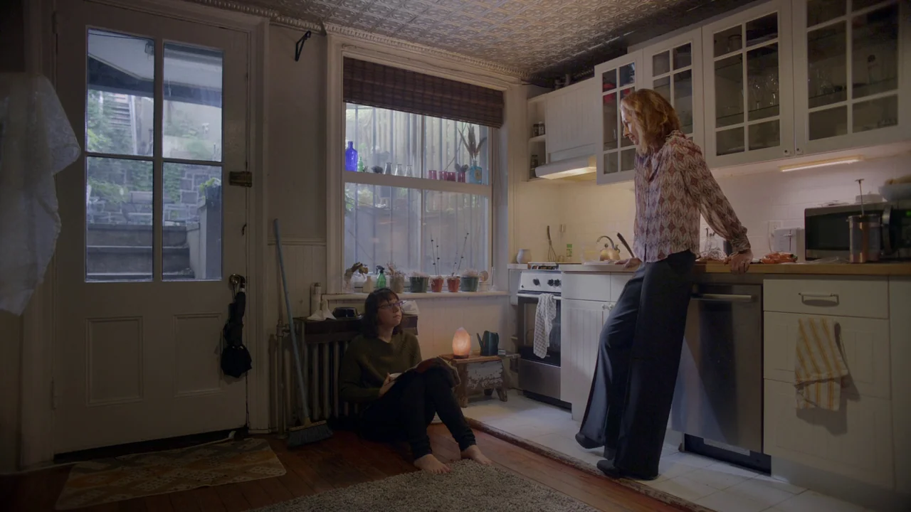 The Feeling That the Time for Doing Something Has Passed (2023) movie still: fullbody — A residential kitchen features white cabinets, patterned…