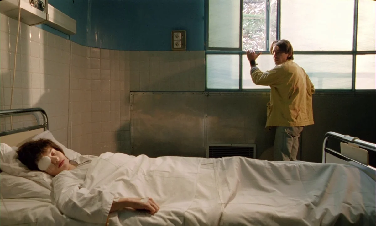 Betty Blue (1986) movie still: wide — A spartan hospital room features tiled blue walls and a metal window frame. A woman with an eye patch sleeps…