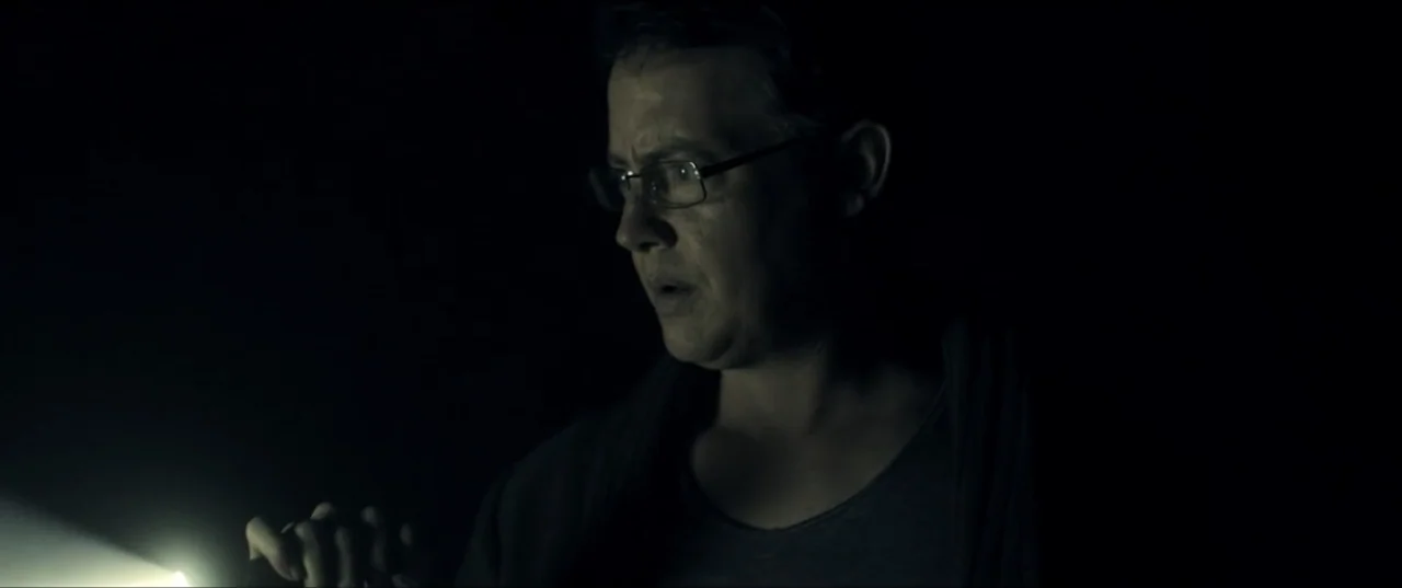 Room 6 (2006) movie still: closeup — A person stands in a completely dark interior space. The subject holds a flashlight in their hand, casting…