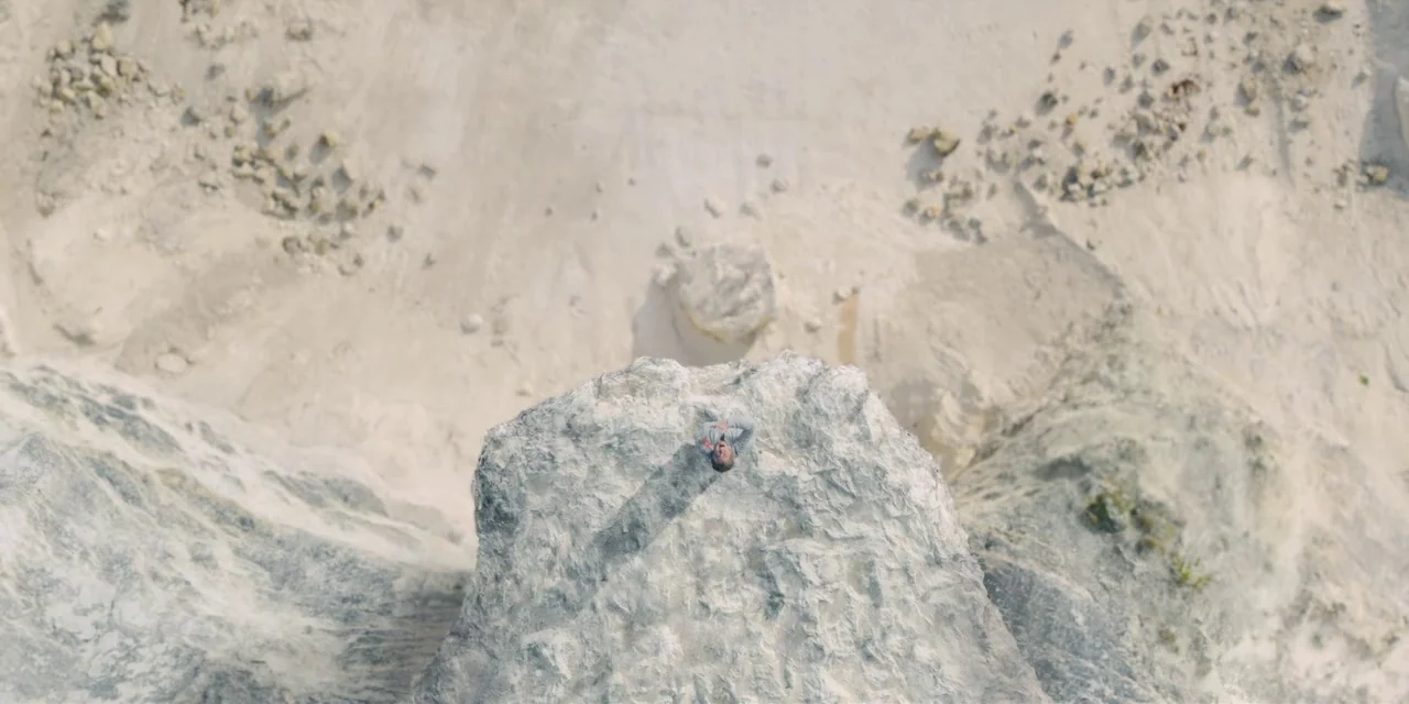 Midsommar (2019) movie still: wide — A vast, eroded chalk quarry features a solitary person resting on a high ledge. The subject lies flat on the…