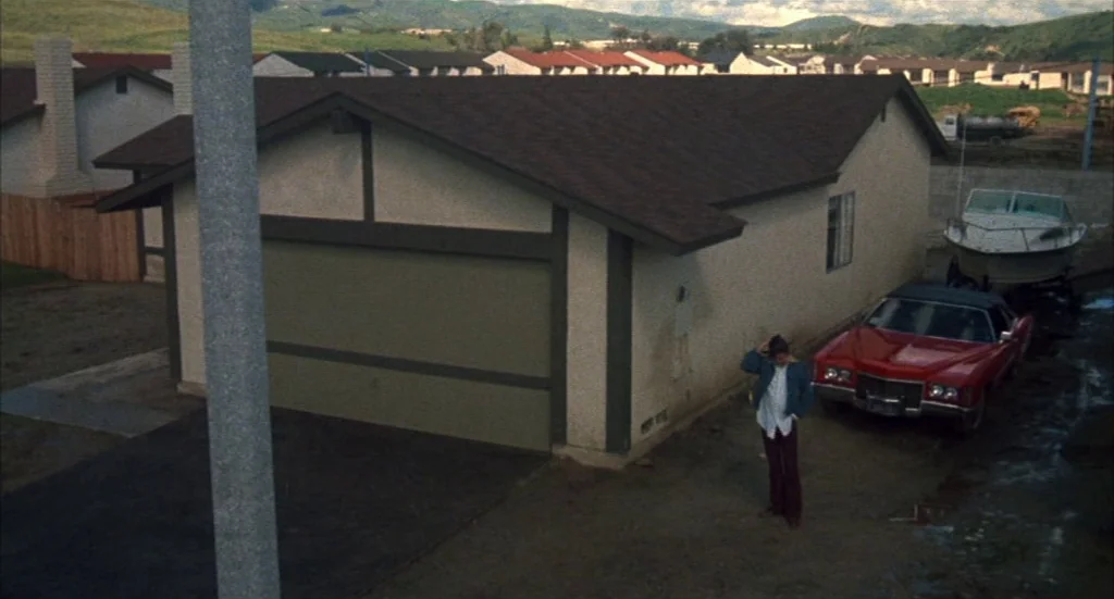 Melvin & Howard (1980) movie still: wide — A stucco house with a dark brown roof sits in a suburban tract development. A man stands beside a red…