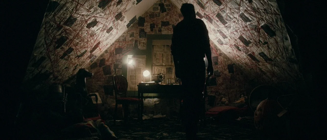 I Trapped The Devil (2019) movie still: fullbody — An attic room features sloped walls covered in papers connected by red string webs. A solitary…