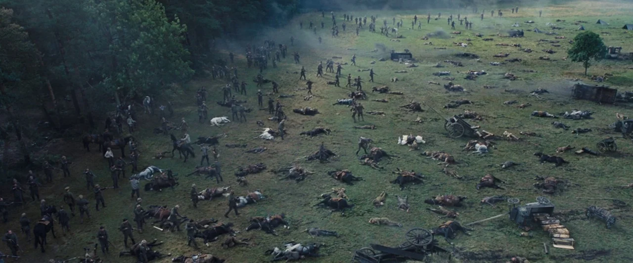 War Horse (2011) movie still: establishing — A sprawling grassy battlefield is littered with numerous fallen horses and soldiers. Survivors in…