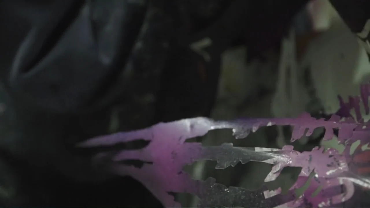 Hondar 2050 (2018) movie still: closeup — A dark indoor space contains a translucent plastic stencil with intricate leaf-like cutouts. The thin…