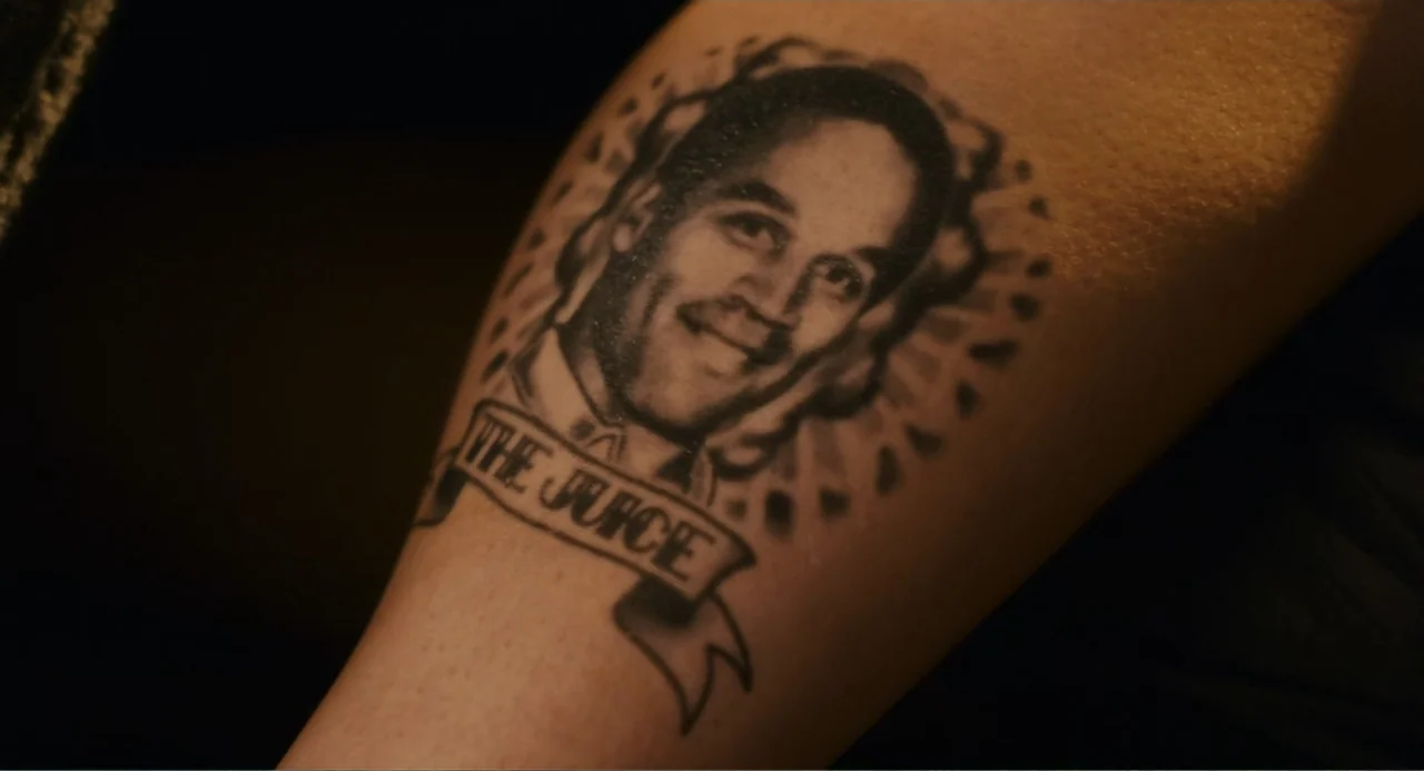 Grown Ups (2010) movie still: closeup — A close-up view shows a black ink tattoo on a person's skin. The tattoo depicts a portrait of a man with a…
