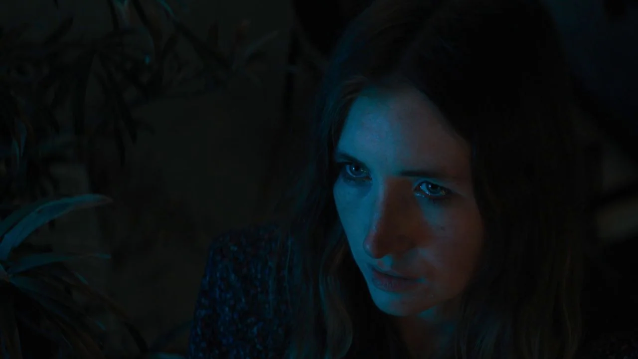 She Dies Tomorrow (2020) movie still: closeup — A dimly lit room is filled with shadow and the faint silhouette of foliage. A young woman stares…