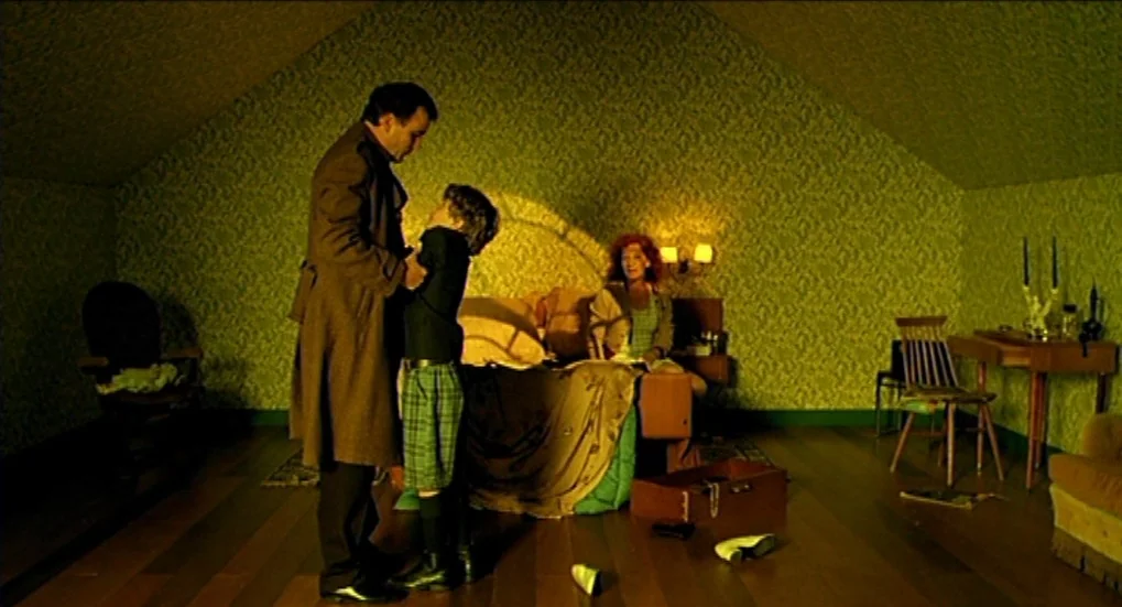 Jeux d’Enfants (2003) movie still: fullbody — An attic with angled ceilings and green patterned wallpaper contains furniture and scattered personal…