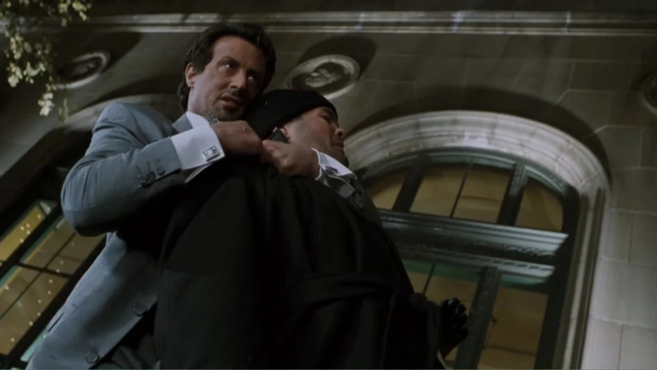 Get Carter (2000) movie still: medium — A stone building exterior with architectural detailing is visible at night. A man in a suit pulls a man in a…