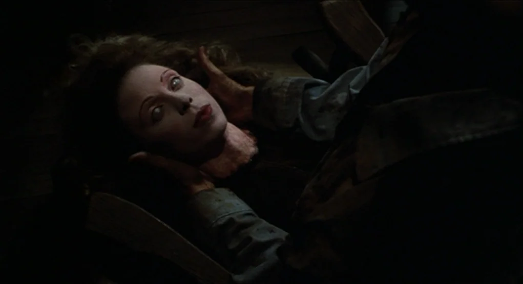 Evil Dead II (1987) movie still: closeup — A dark interior space features a pale woman lying on a wooden surface. A person's hands cradle her head…