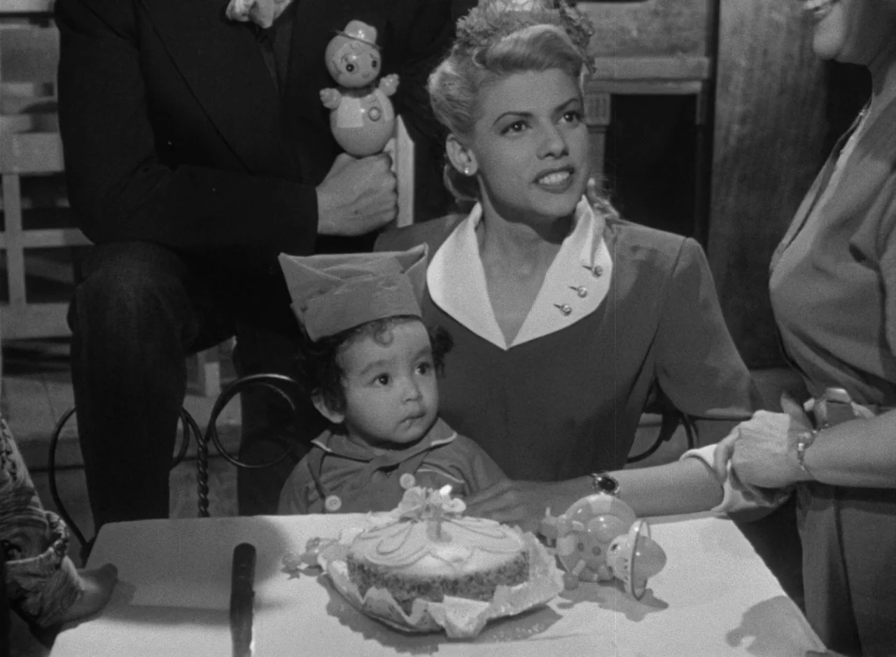 Victims of Sin (1951) movie still: medium — A birthday celebration takes place at a table with a lit cake. An adult woman sits with a small child…