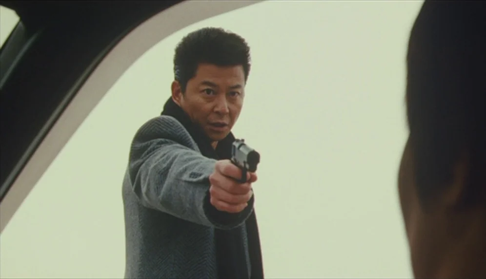 Gozu (2003) movie still: medium — An over-the-shoulder view from inside a vehicle looking toward an armed man. The background is a bright,…