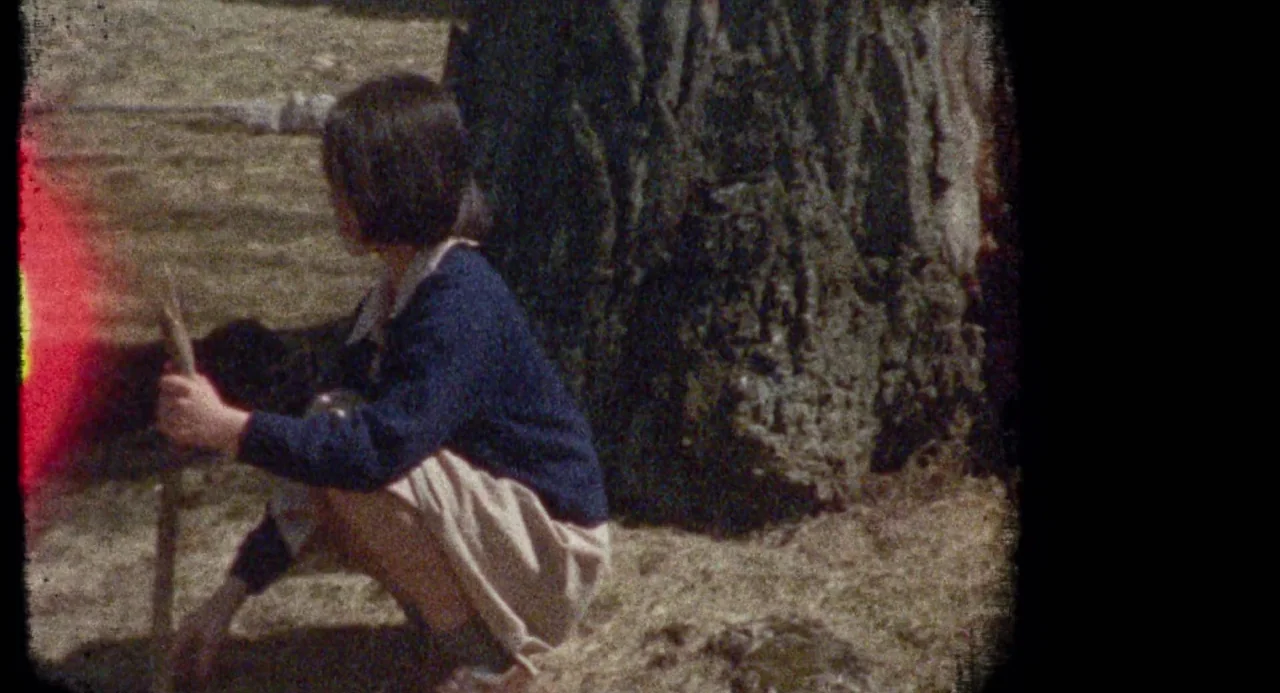 Martyrs (2008) movie still: medium — A girl crouches beside a large tree trunk in an open, grassy field. She holds a thin wooden stick in her hands…