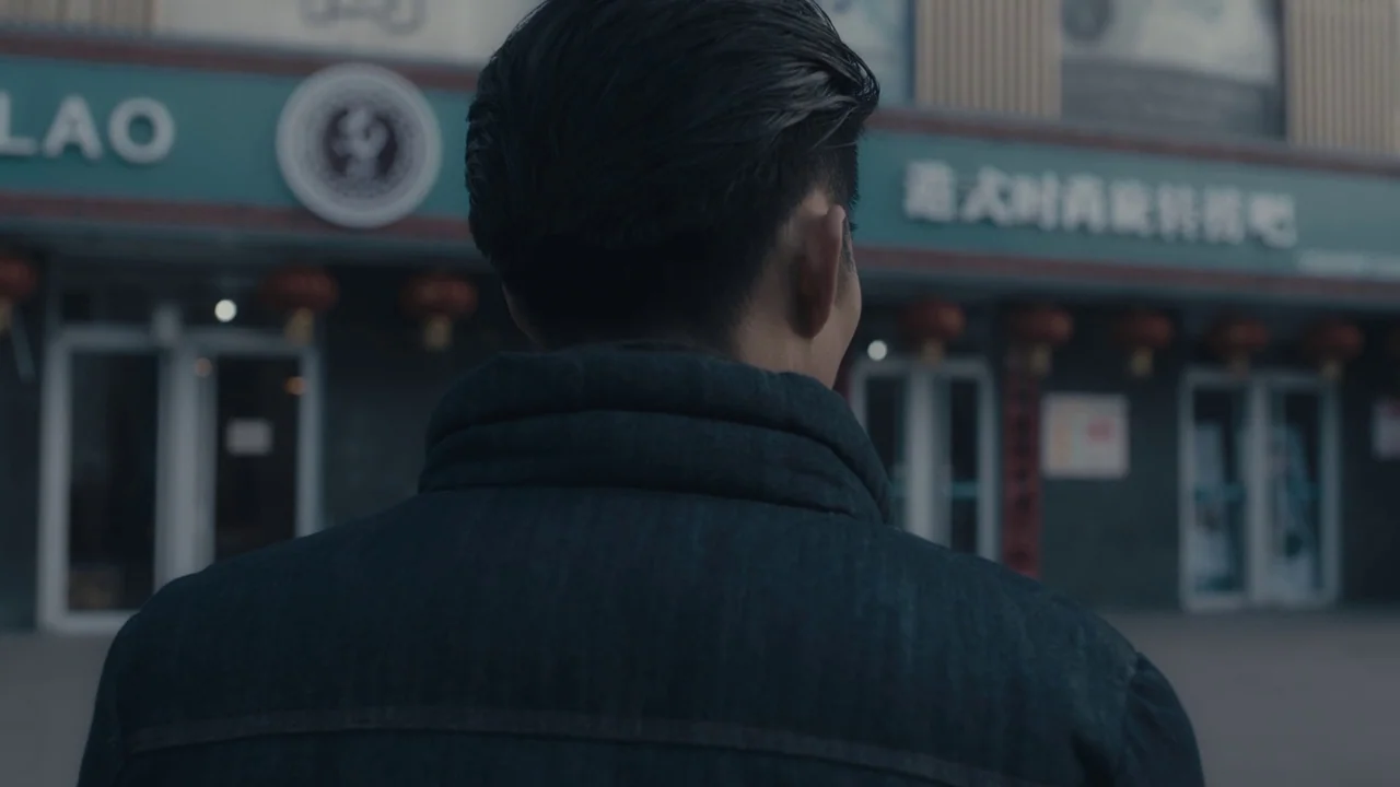 An Elephant Sitting Still (2018) movie still: medium — A man stands in front of a building with teal signage and red lanterns. The man looks ahead…