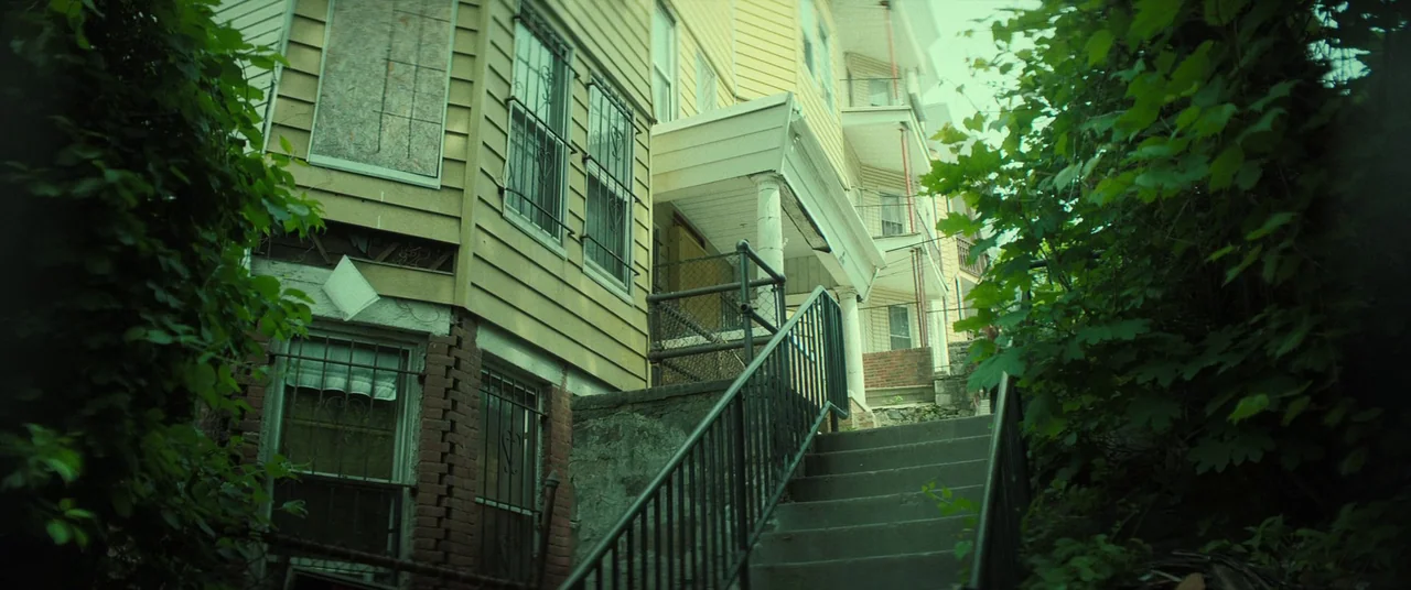 The Many Saints of Newark (2021) movie still: establishing — A multi-story residential building with yellow siding and metal window security grates…