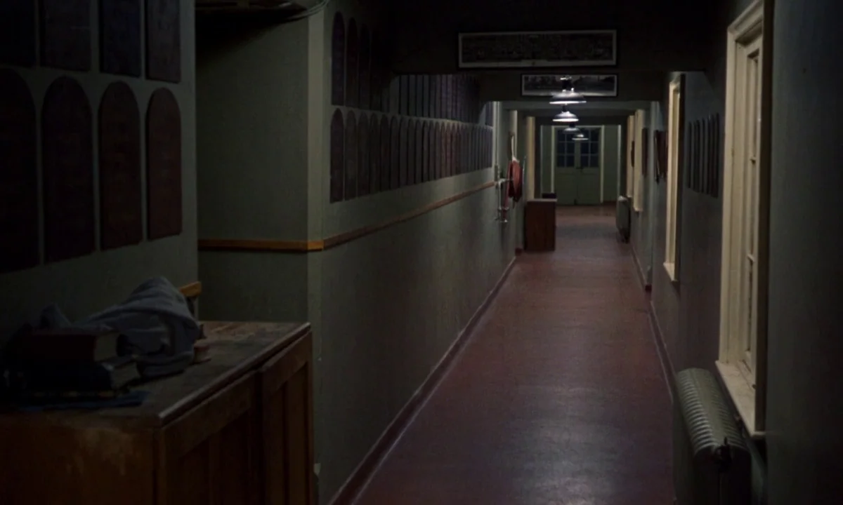 If…. (1968) movie still: establishing — A long dim hallway lined with dark wooden memorial plaques on the walls. The floor is covered in red…
