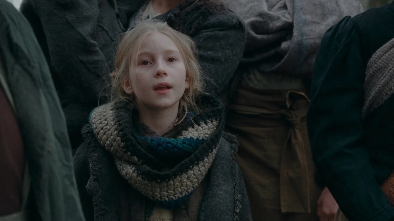 The Devil’s Bath (2024) movie still: medium — A group of people dressed in worn, textured period clothing stands outdoors. A young girl with blonde…