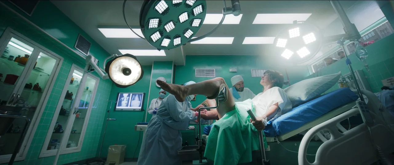 Bardo: False Chronicle of a Handful of Truths (2022) movie still: medium — A green-tiled delivery room with large hanging surgical lights overhead.…