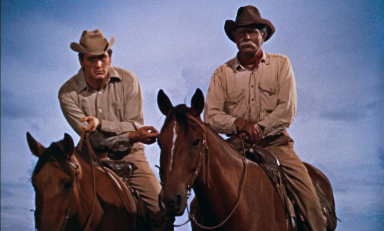 Giant (1956) movie still: medium — Two men on horseback stand against a wide expanse of pale blue sky. They wear traditional ranch clothing and hats…