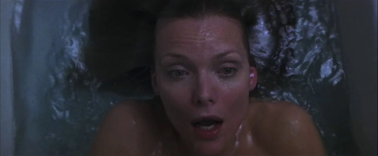 What Lies Beneath (2000) movie still: closeup — A close-up of a woman lying fully submerged in a dark-water bathtub. She gazes directly upward with…