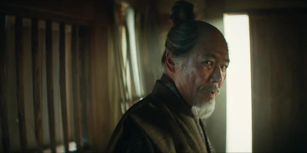 Shogun (2024) movie still: medium — A dimly lit room with vertical wooden slat screens and architectural wooden beams. An elderly man with a topknot…