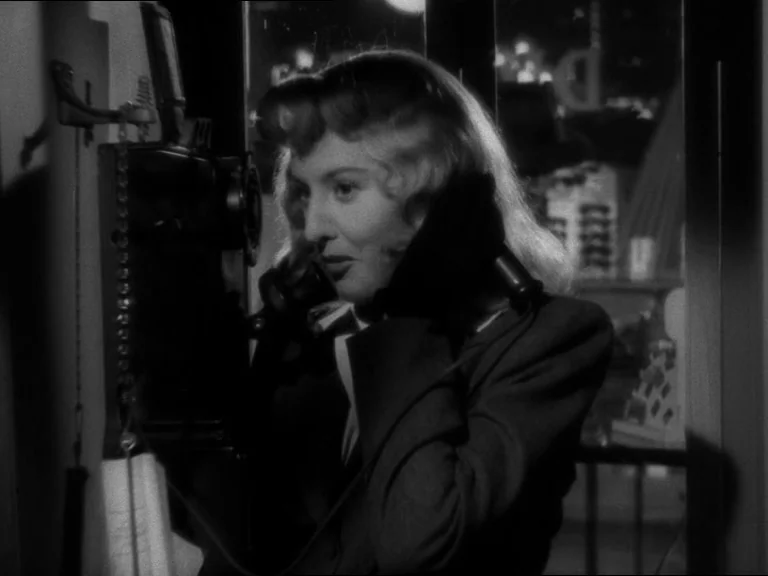 Double Indemnity (1944) movie still: closeup — A dark, cramped phone booth interior at night with a wall-mounted vintage telephone. A woman with…