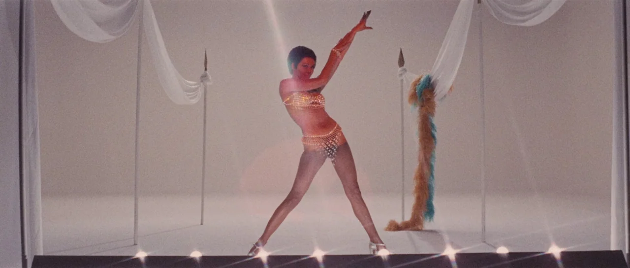 Death Walks On High Heels (1971) movie still: fullbody — A minimalist white studio set features white fabric drapes hanging on simple metal poles. A…