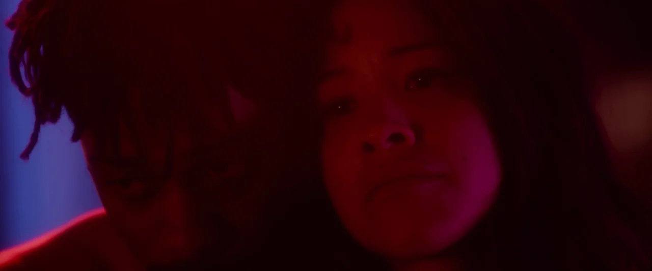 Someone Great (2019) movie still: closeup — A dark indoor space is illuminated by vibrant red and blue neon light sources. A young man with…