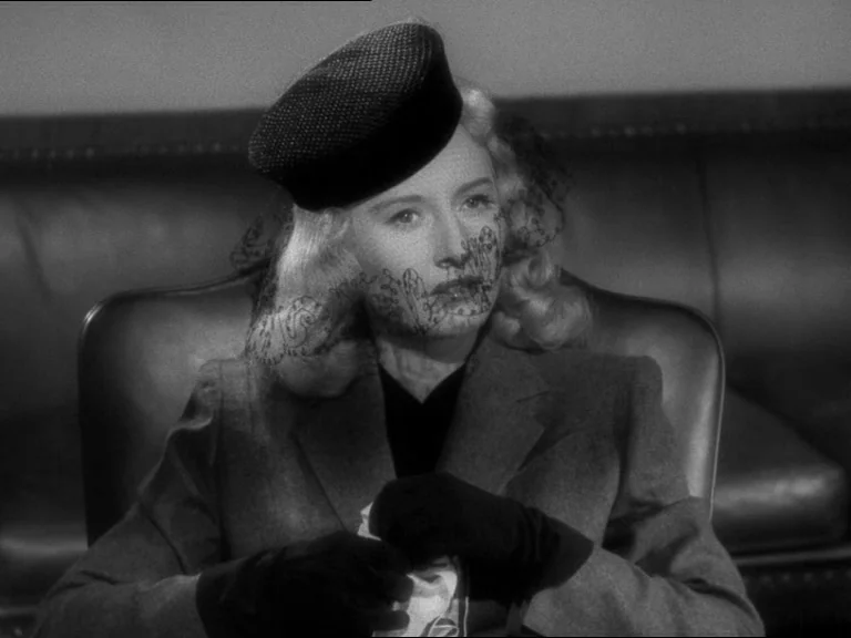Double Indemnity (1944) movie still: medium — A woman sits in a leather chair inside a professional office setting. She holds a white cloth while…