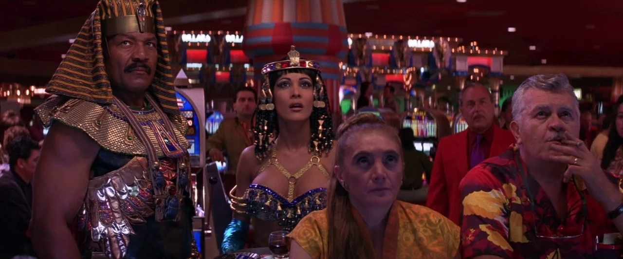 Mars Attacks! (1996) movie still: medium — A dimly lit casino floor with rows of flashing slot machines in the background. A group of people dressed…