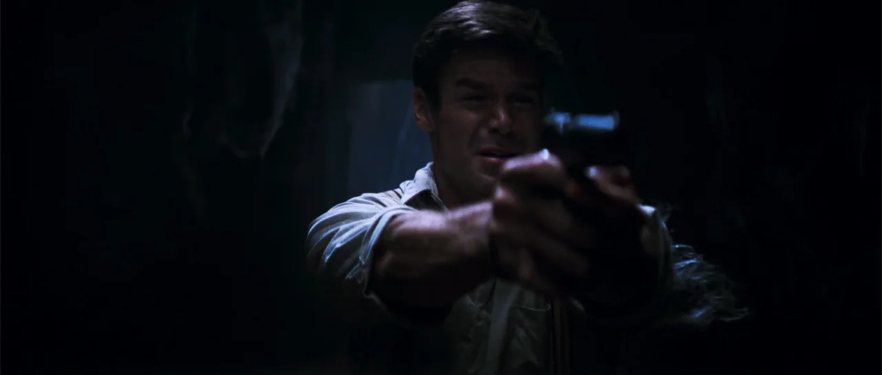 The Mummy (1999) movie still: medium — A dark, unidentifiable interior space with minimal background detail visible due to low lighting. A man…