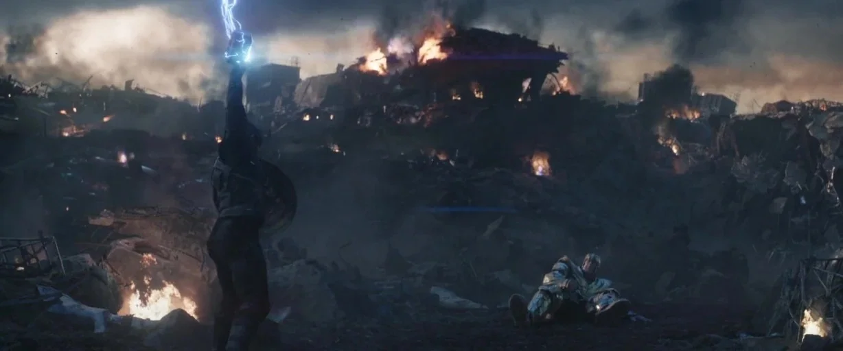 Avengers: Endgame (2019) movie still: wide — A vast, desolate landscape filled with burning wreckage and thick clouds of dark smoke. A man in…