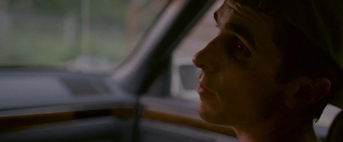The Fighter (2010) movie still: closeup — Inside a vehicle looking toward the window with a blurred outdoor background. A man sits in the driver's…