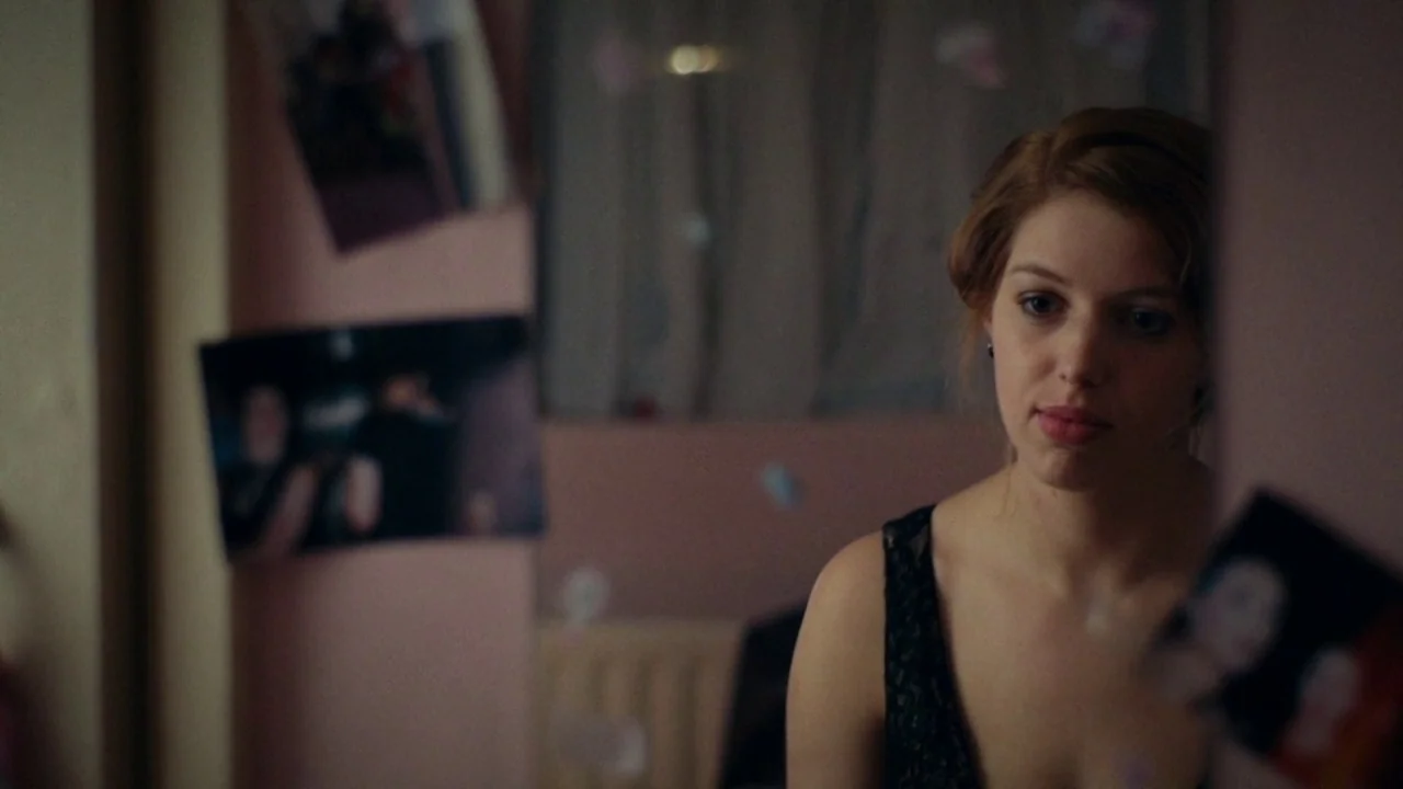 A Date for Mad Mary (2016) movie still: medium — A dimly lit room with pink walls is decorated with unframed photographs taped to surfaces. A young…