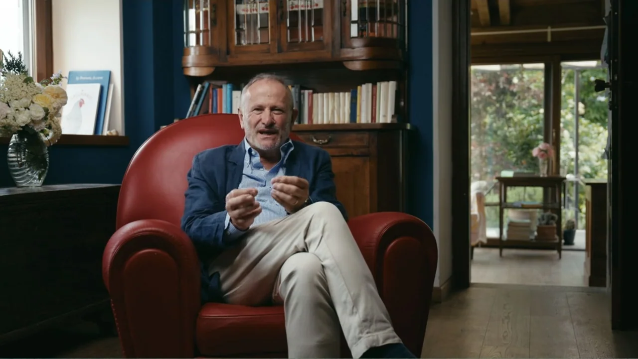 FRAGILE - The story of Nicolò Fagioli (2024) movie still: medium — A man sits in a red leather armchair inside a home living room. He is talking…