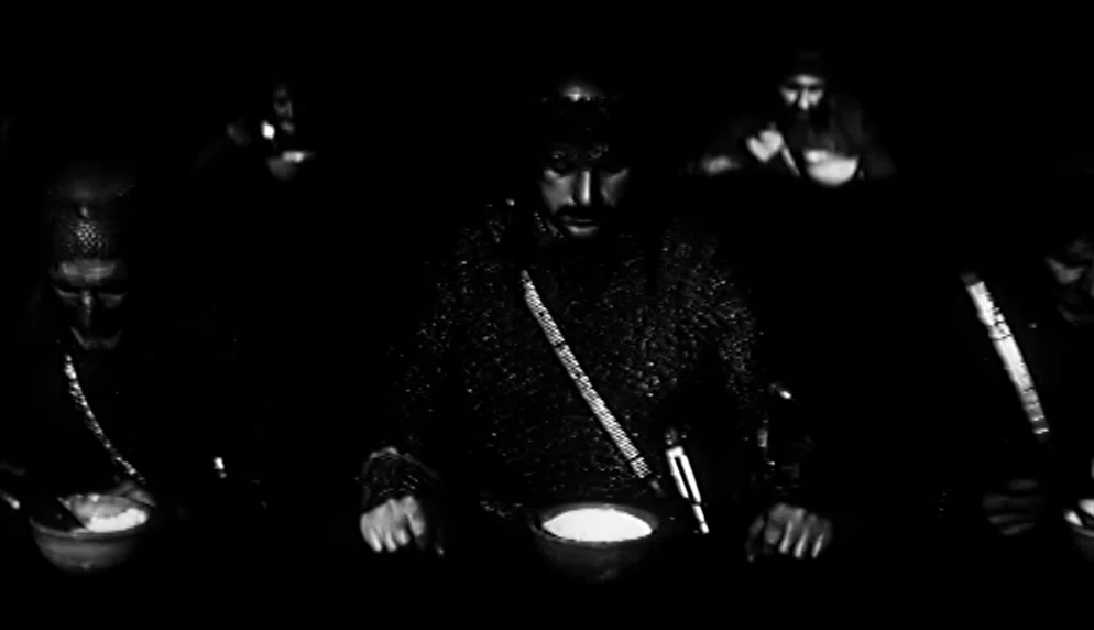 The Plea (1968) movie still: medium — A dark space where men in chainmail sit at a table eating from bowls. The only visible light sources highlight…