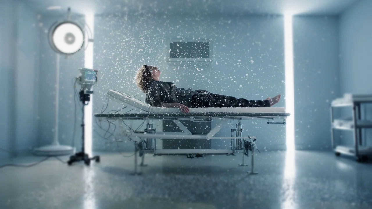 Cult of Chucky (2017) movie still: fullbody — A clinical examination room with bright blue walls and minimalist medical furniture. A person lies…