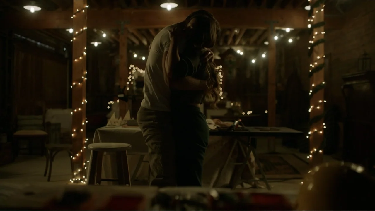 A Carpenter Christmas Romance (2024) movie still: medium — A dimly lit rustic workshop is decorated with string lights wrapped around wooden posts.…