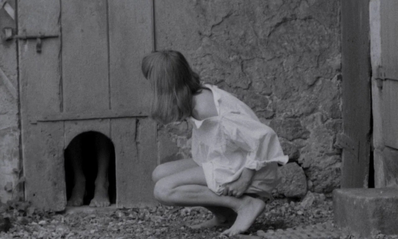 The Secret Son (1979) movie still: medium — An outdoor area features a rustic stone wall and a weathered wooden door. A young girl in a…