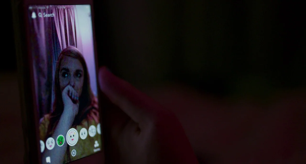 Eighth Grade (2018) movie still: closeup — A dimly lit room is illuminated by the bright screen of a mobile phone. A person holds the device while…