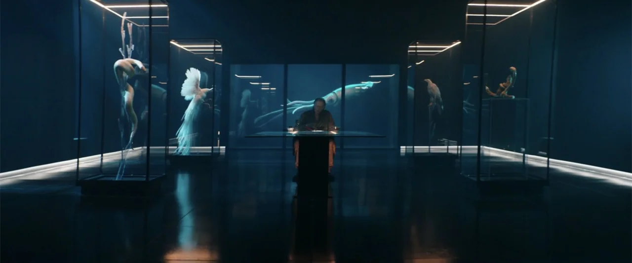 Jolt (2021) movie still: wide — A dark gallery features multiple illuminated glass display cases holding various natural history specimens. An older…