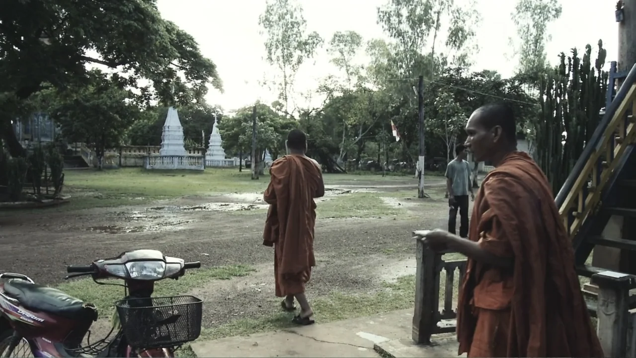 A Cambodian Spring (2018) movie still: medium — An outdoor courtyard of a Buddhist temple features white stupas and lush green trees. One monk walks…