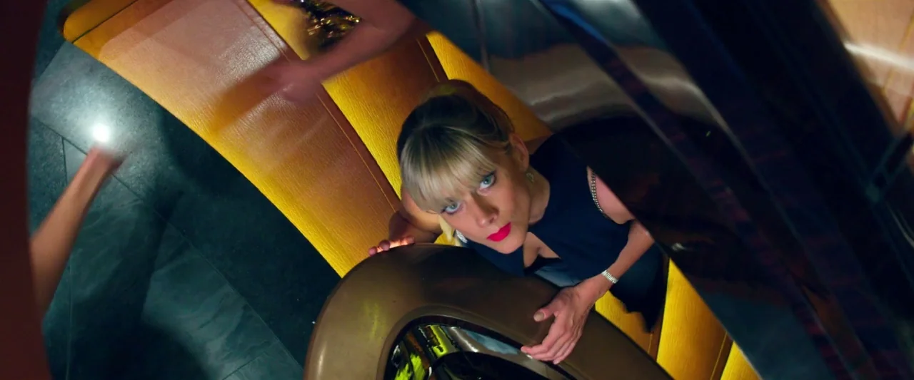 6 Underground (2019) movie still: medium — A dark staircase features bright yellow lit steps with a curved metal banister. A blonde woman in a dark…