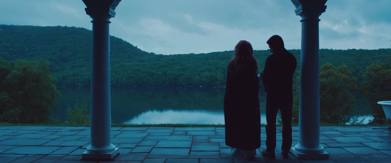 Kiss of the Damned (2012) movie still: wide — A stone-paved patio framed by white classical pillars overlooks a calm lake and forest. A man and…